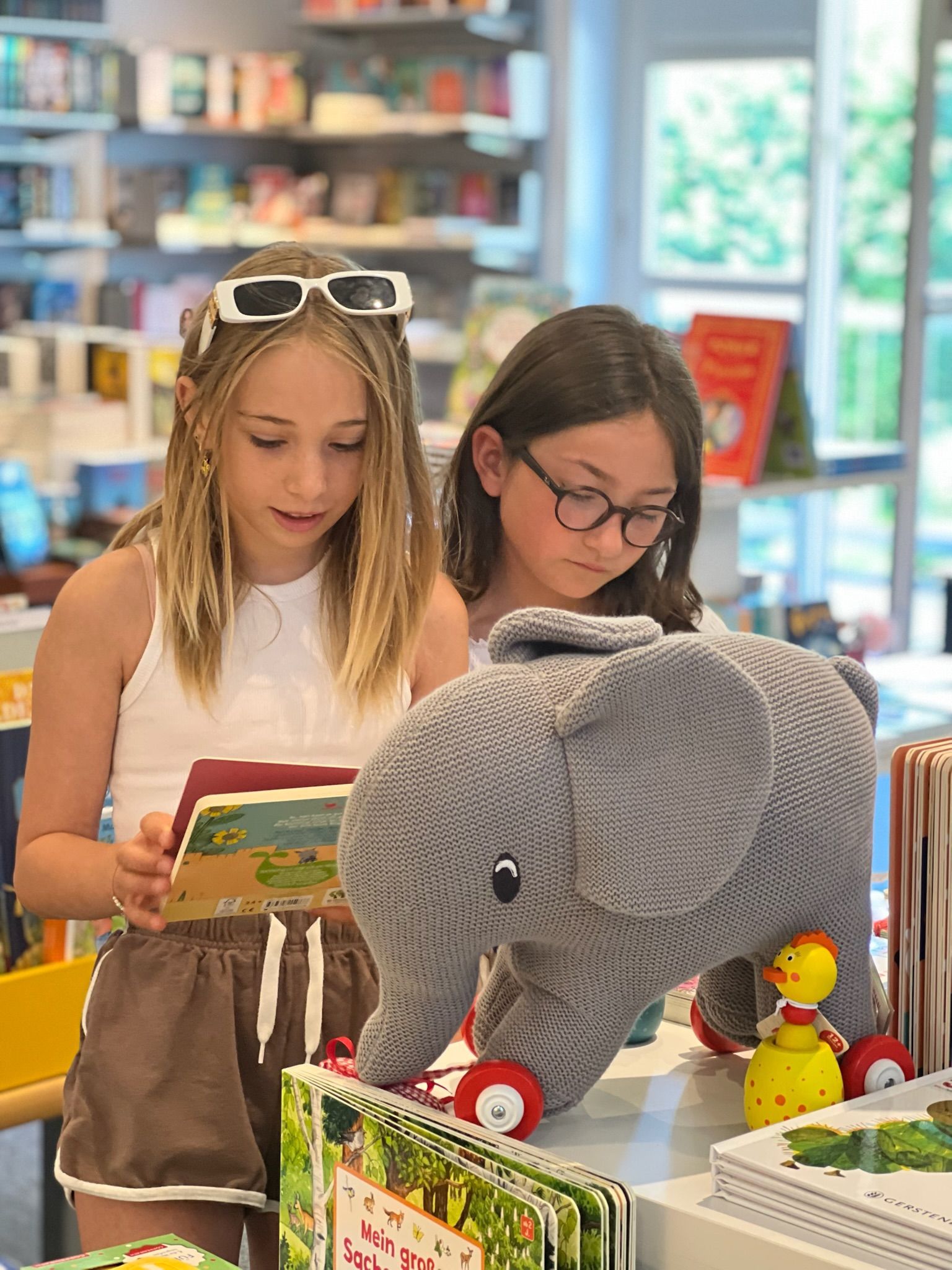 Zwei Mädchen schmökern mit Plüschelefant in der Buchhandlung Rupprecht Zwei Mädchen schmökern mit Plüschelefant in der Buchhandlung Rupprecht